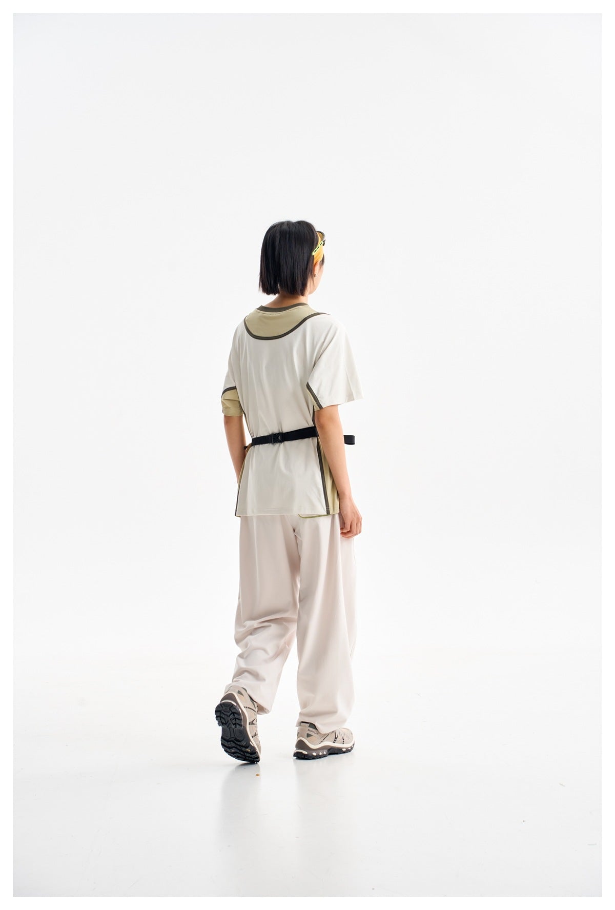 Model shown from behind wearing a white short-sleeve shirt with olive and dark trim and loose light pants.