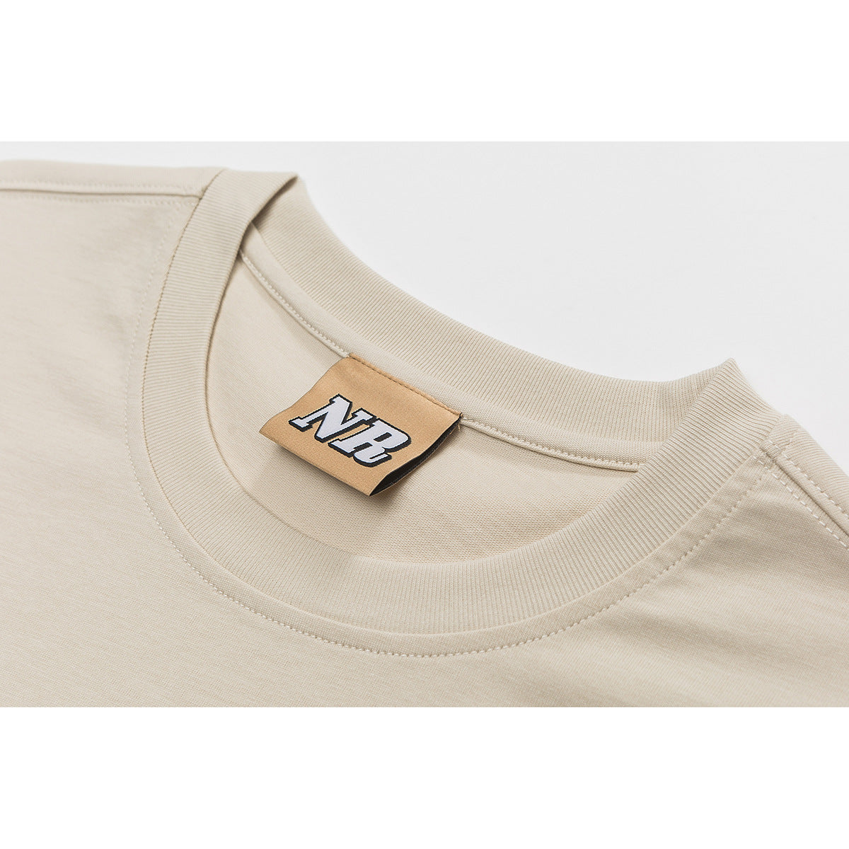 Close-up of a cream T-shirt's ribbed crew neck, stitching, and tan NR neck label.