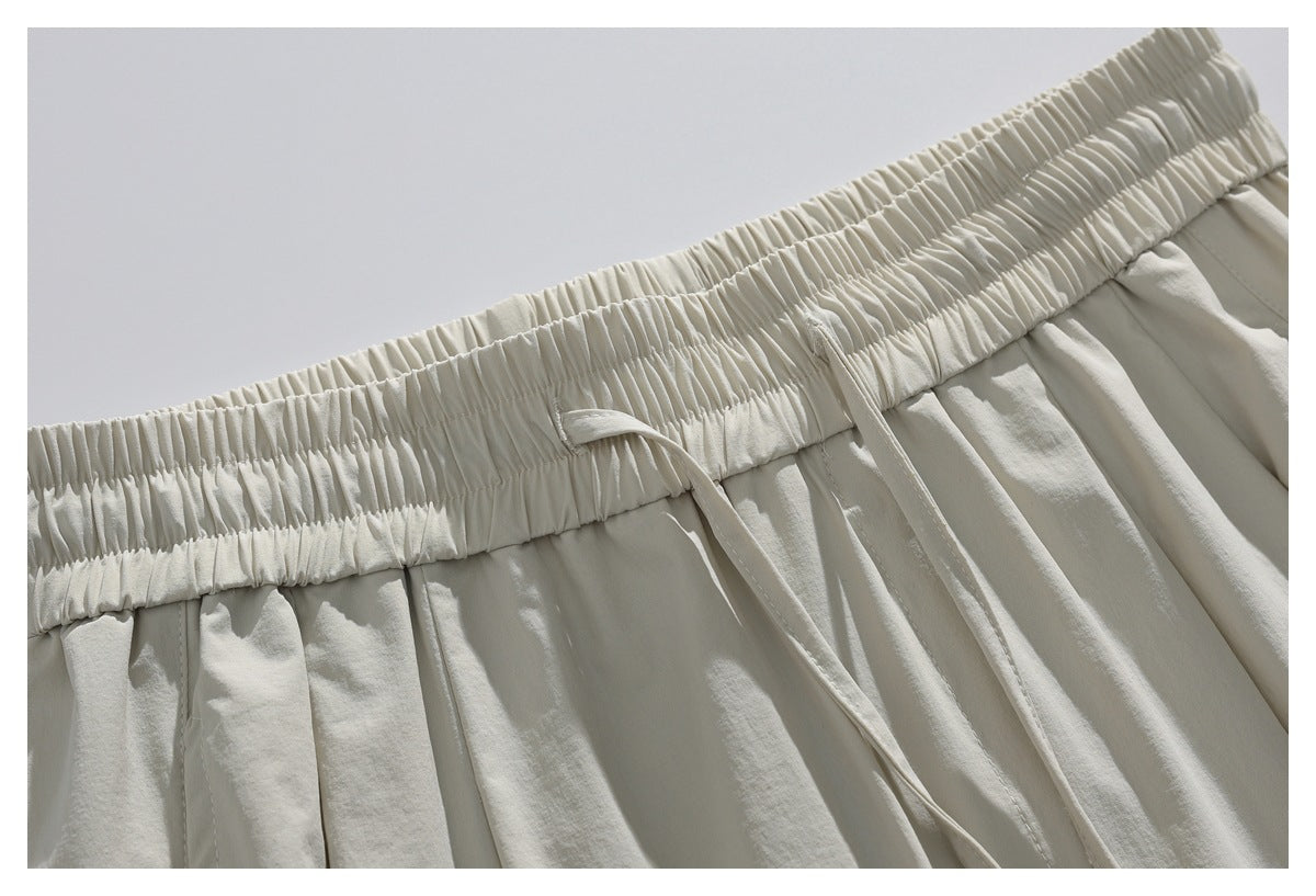 Close-up of off-white trousers with a wide gathered elastic waistband, front pleats, and a hanging drawstring.
