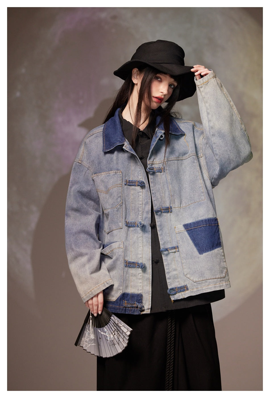 Closer front view of a model wearing a gray denim jacket with blue contrast patches, oversized sleeves and loop closures.