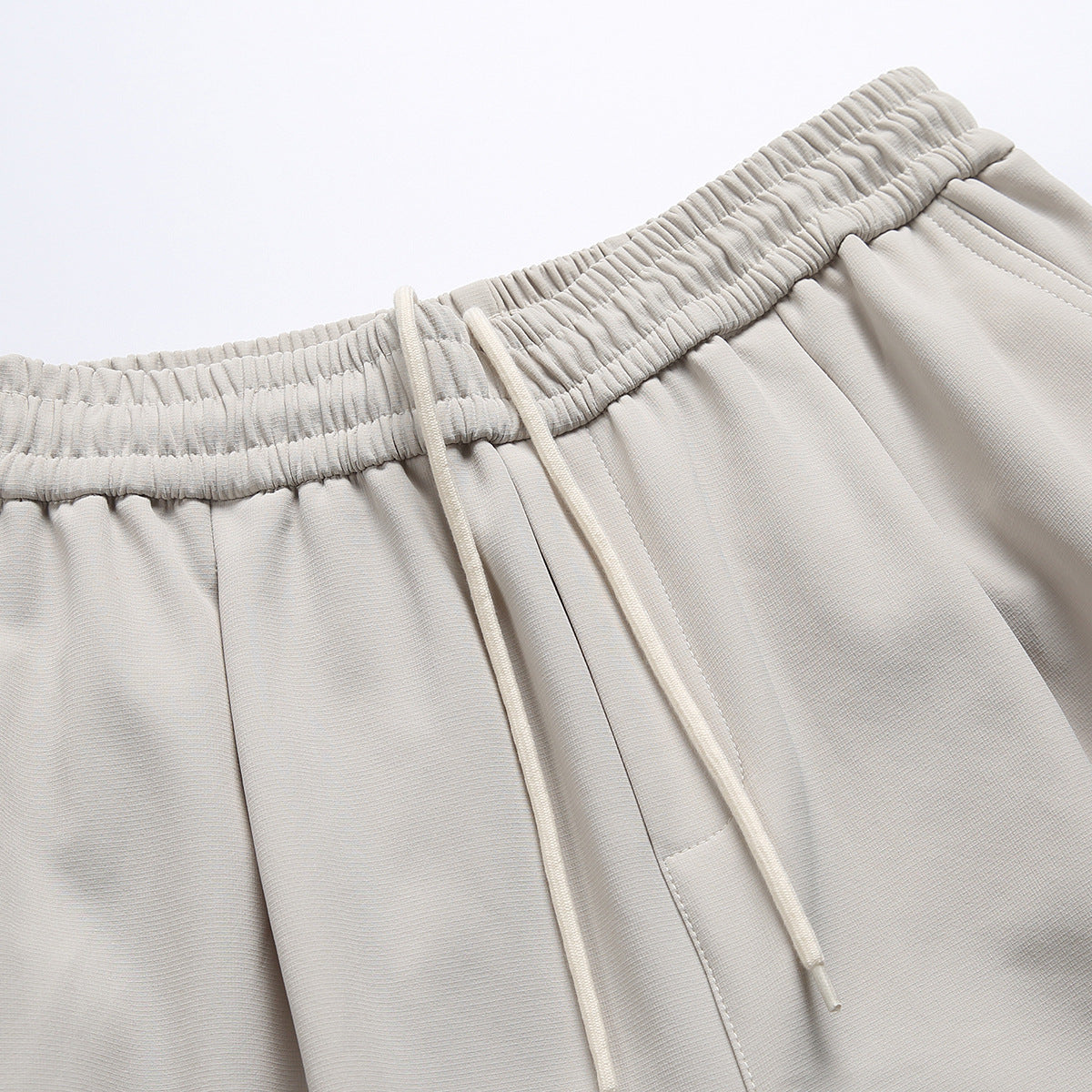 Close-up of light beige trousers with a gathered elastic waistband and long matching drawstrings.