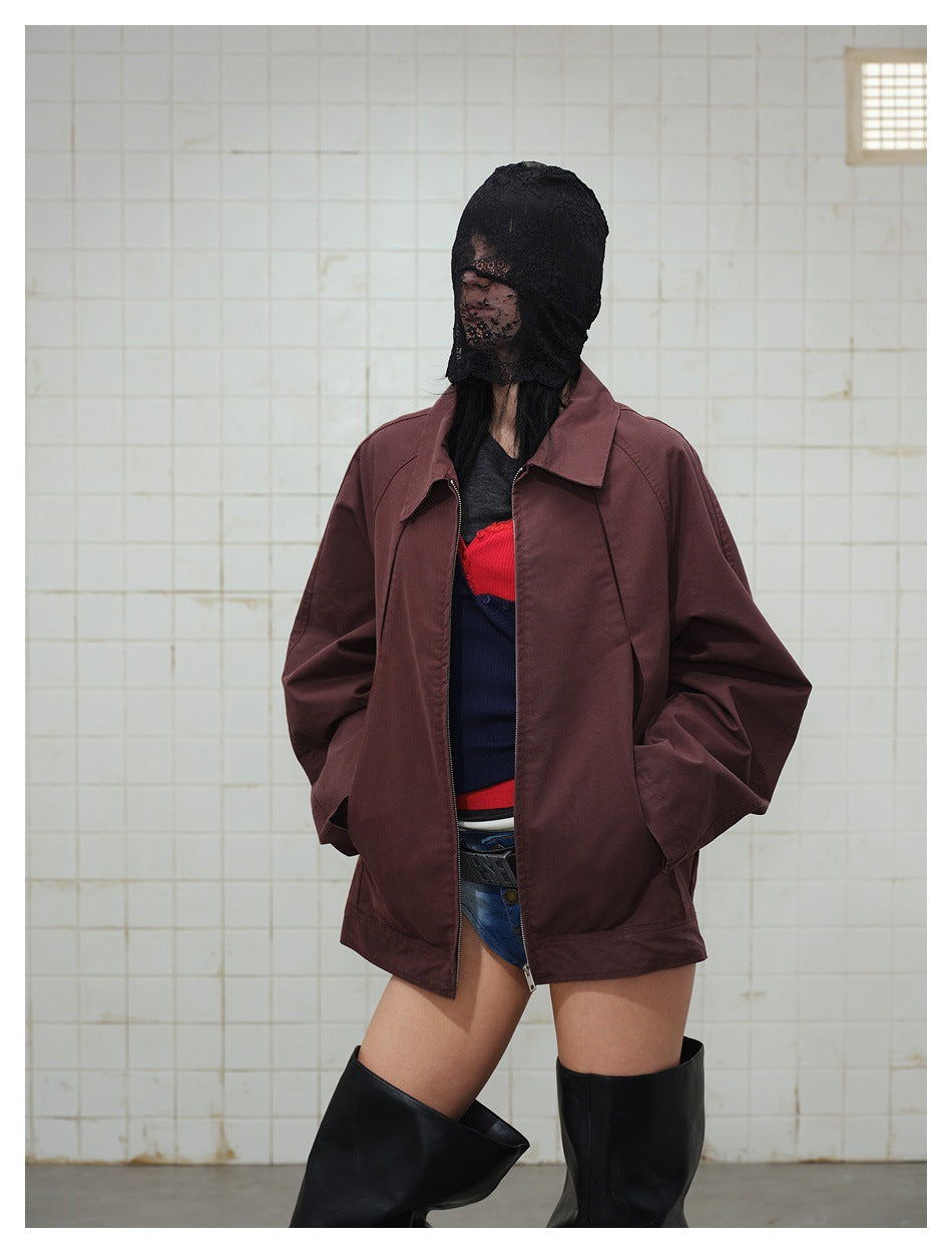 Model in a wine-red zip jacket worn open with hands in pockets, lace head covering and black boots, tiled wall
