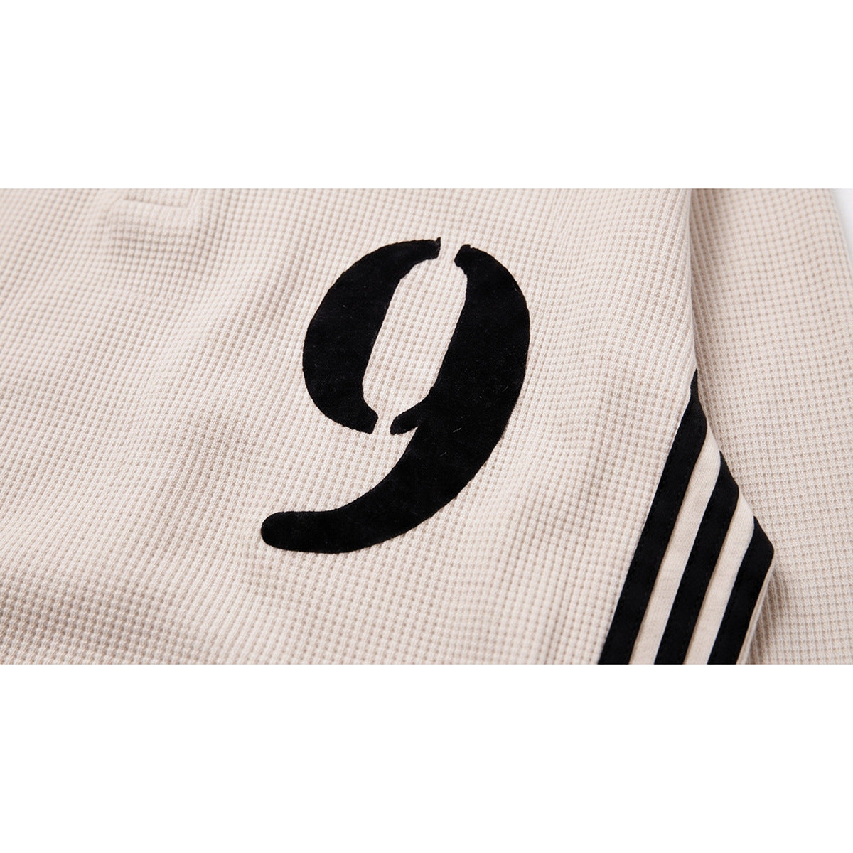 Close-up of a black number 9 graphic and stripe detail on cream waffle-textured fabric.