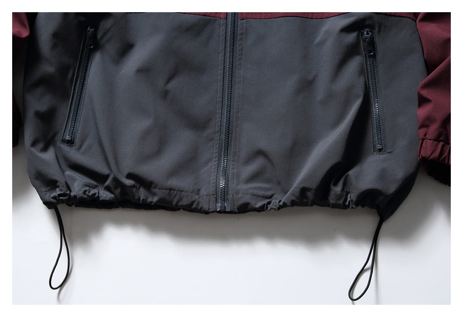 Close-up of the jacket’s charcoal lower front, showing two zip pockets, center zipper and adjustable hem cords.