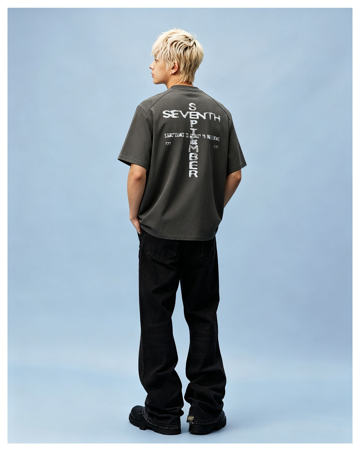 Person seen from behind wearing the gray-green T-shirt with back graphic, black baggy jeans and black boots