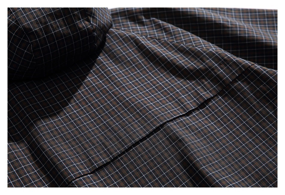 Close-up of dark charcoal plaid fabric with thin white and rust-colored lines, softly folded and draped.
