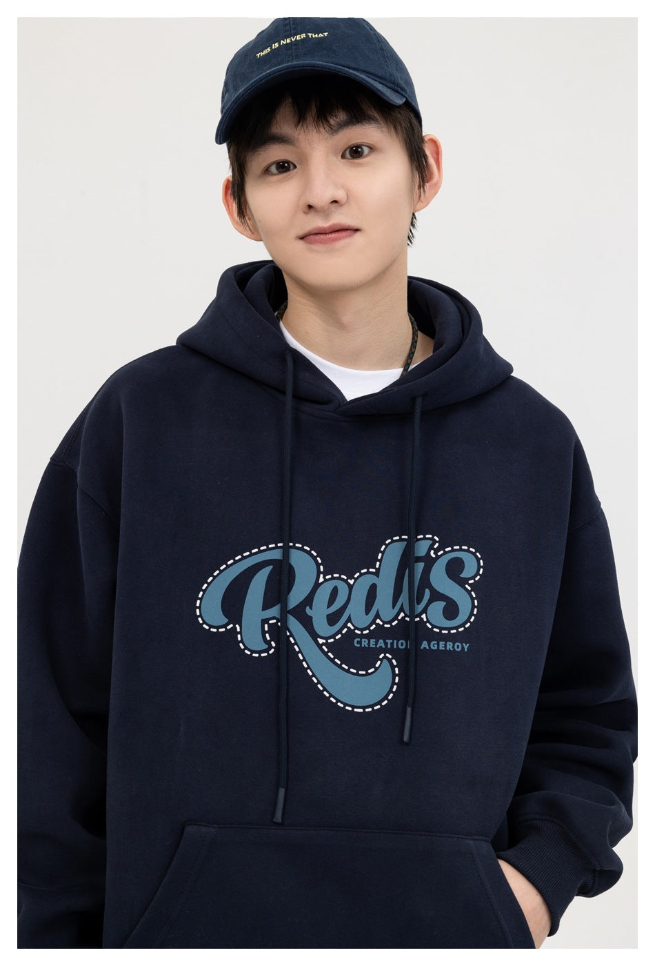 Model wearing a navy pullover hoodie with a blue-and-white chest graphic and a navy cap.
