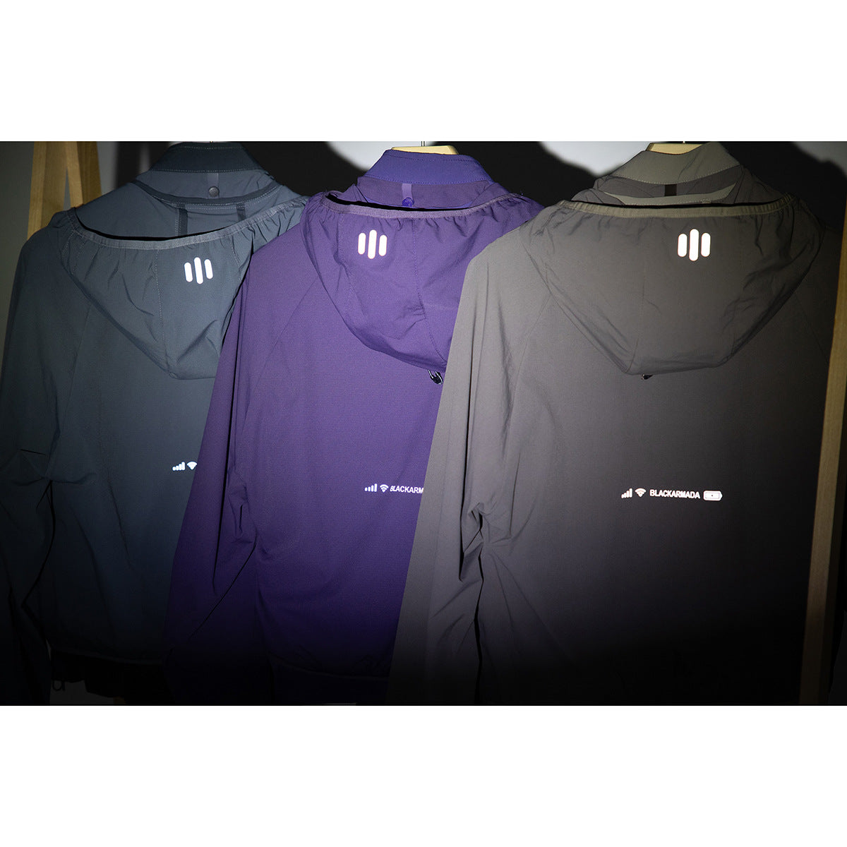 Three hooded jackets shown from the back in charcoal, purple, and taupe; the image is dark with wide white borders.
