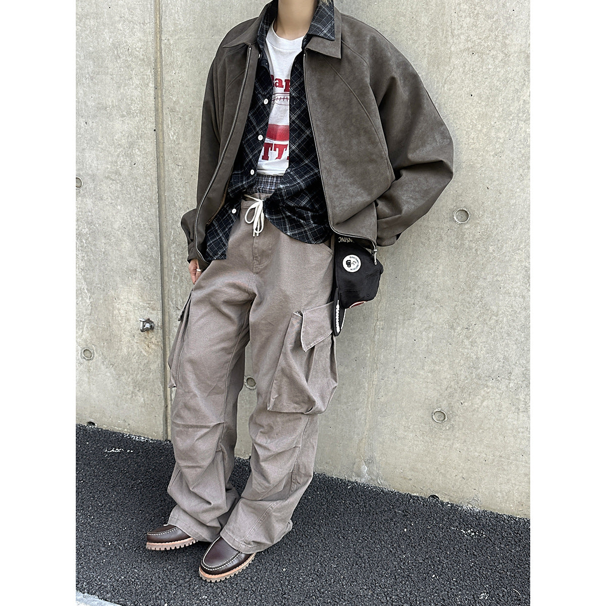 Model wearing loose taupe cargo pants with oversized flap pockets, styled with a gray jacket and plaid shirt.