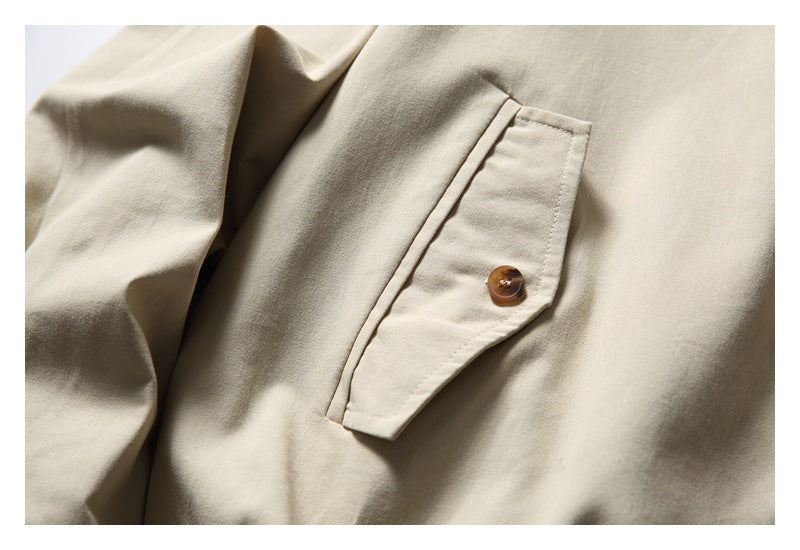 Close-up of a beige jacket pocket flap with a brown button and visible stitching.