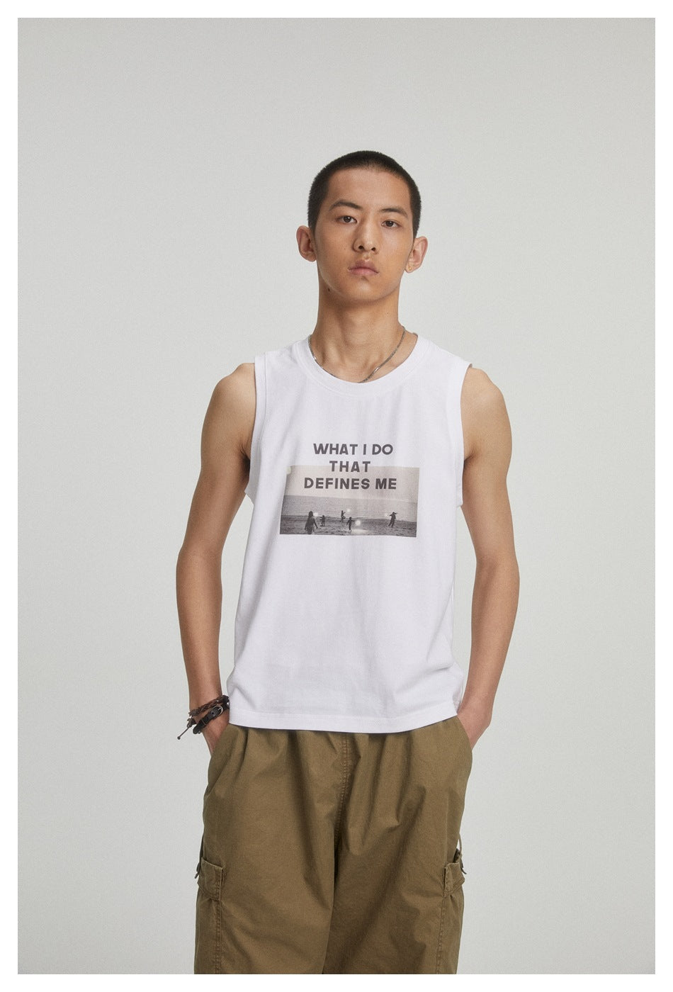 Model wearing a white sleeveless shirt with a text-and-beach-photo graphic and olive cargo pants.