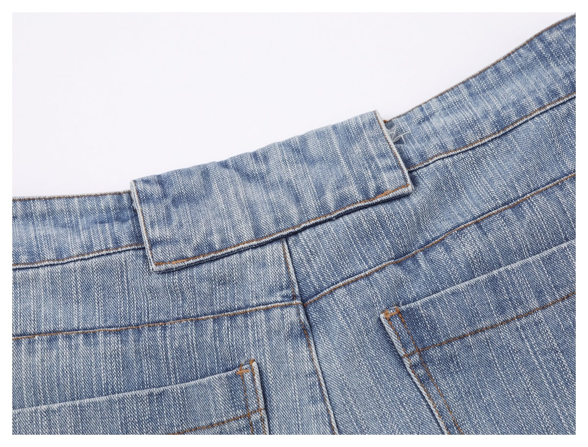 Close-up of light blue denim trousers showing the waistband, belt loop, and contrast stitching.