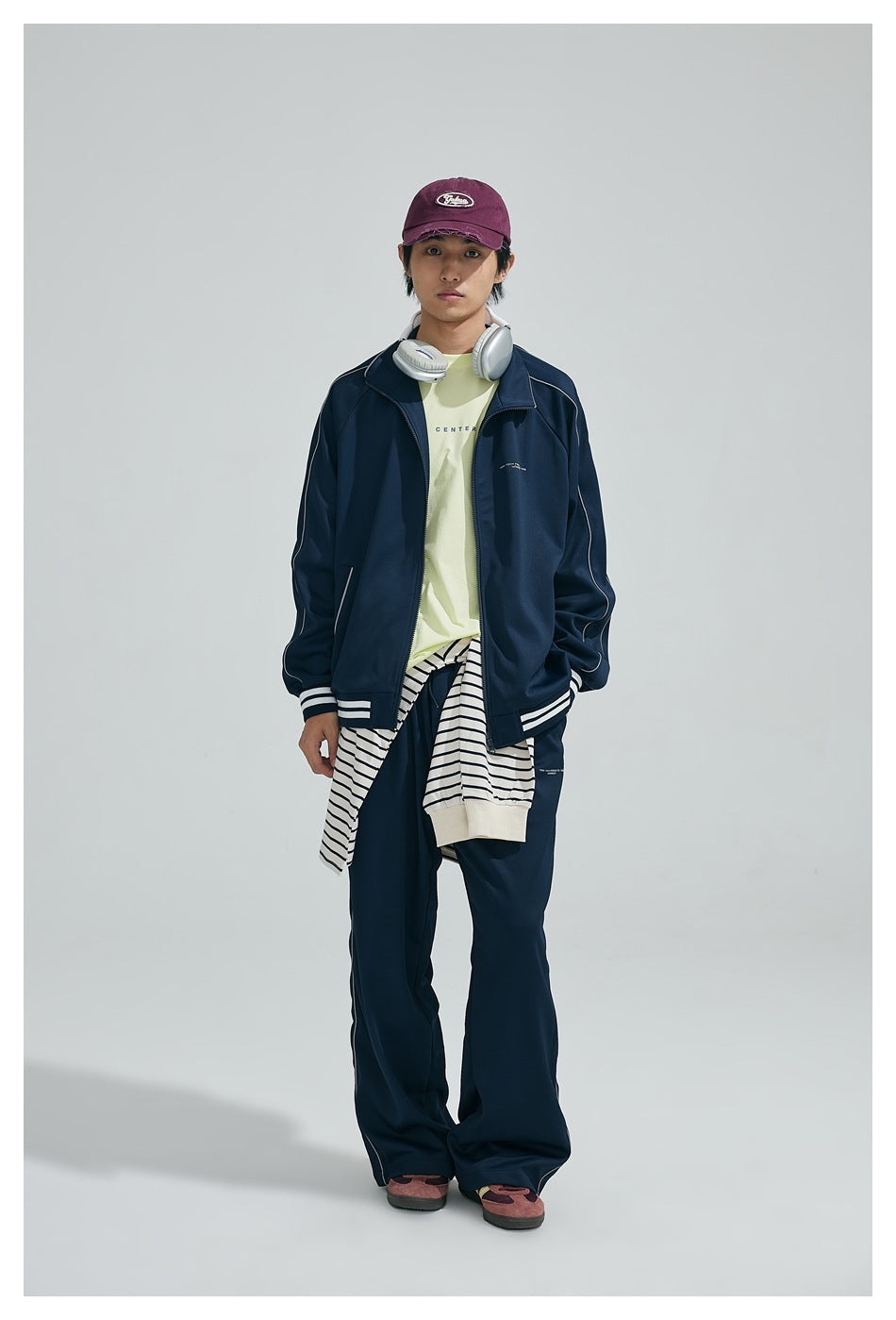 Model wearing navy stand-collar zip jacket with white-striped cuffs and hem, matching pants, maroon cap and headphones