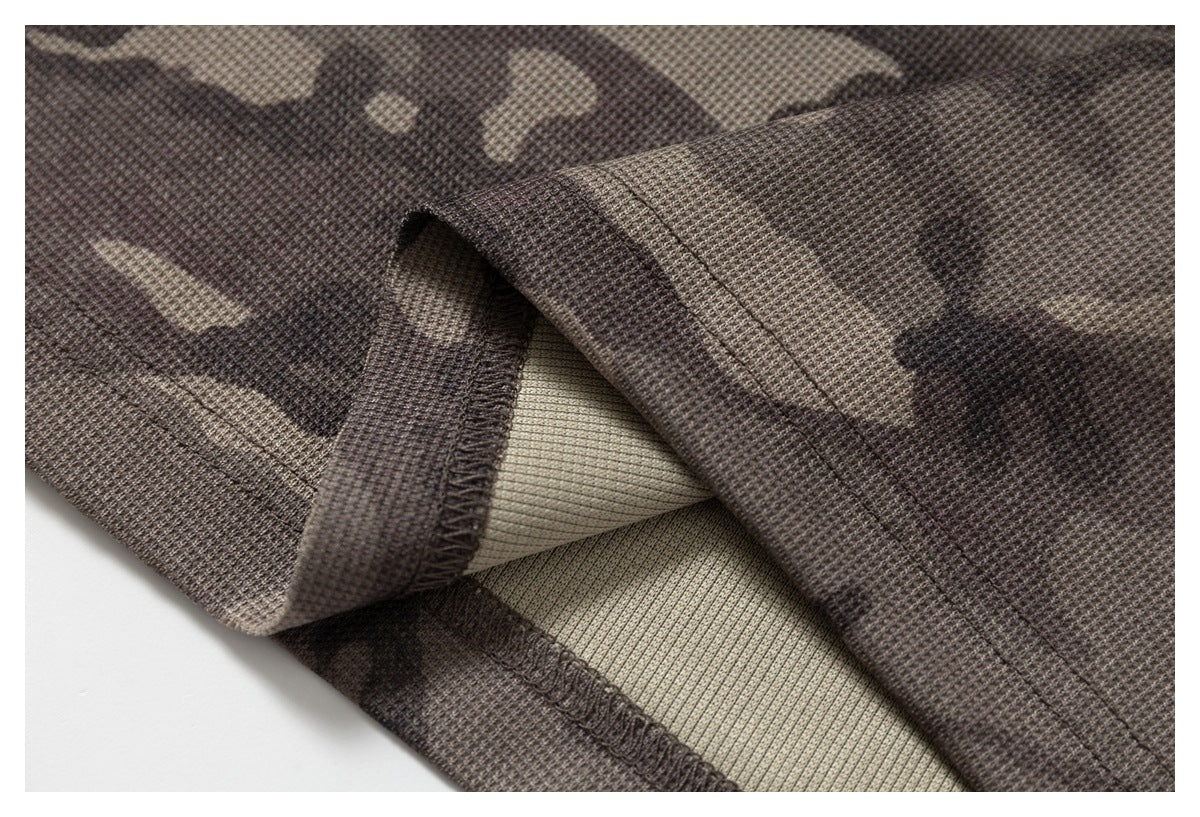 Close-up of brown and tan camouflage fabric showing a folded edge, stitching, and inner lining.