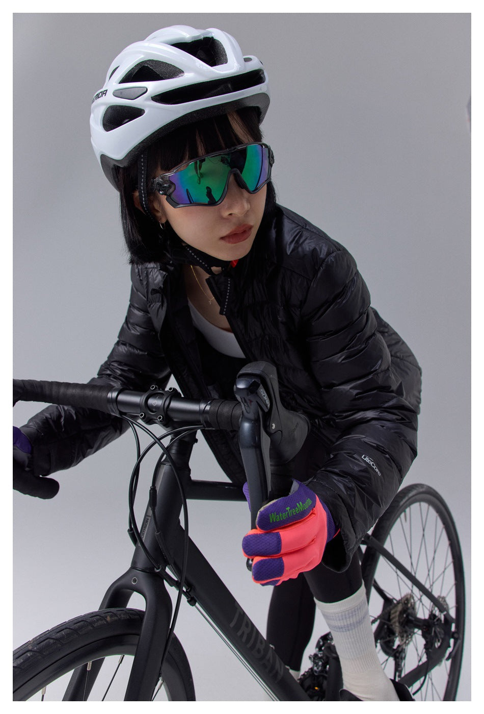 Close-up of model in black quilted jacket, helmet, sunglasses and gloves leaning on bike handlebars