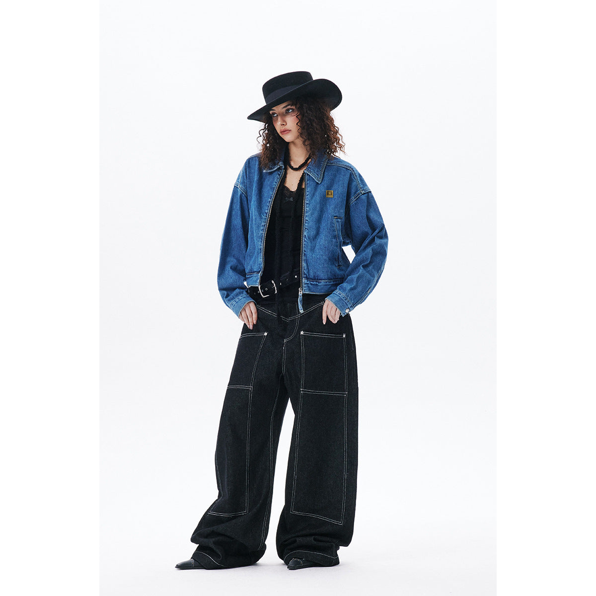 Full-length front view of a model wearing a blue denim jacket and black wide-leg jeans with contrast stitching.