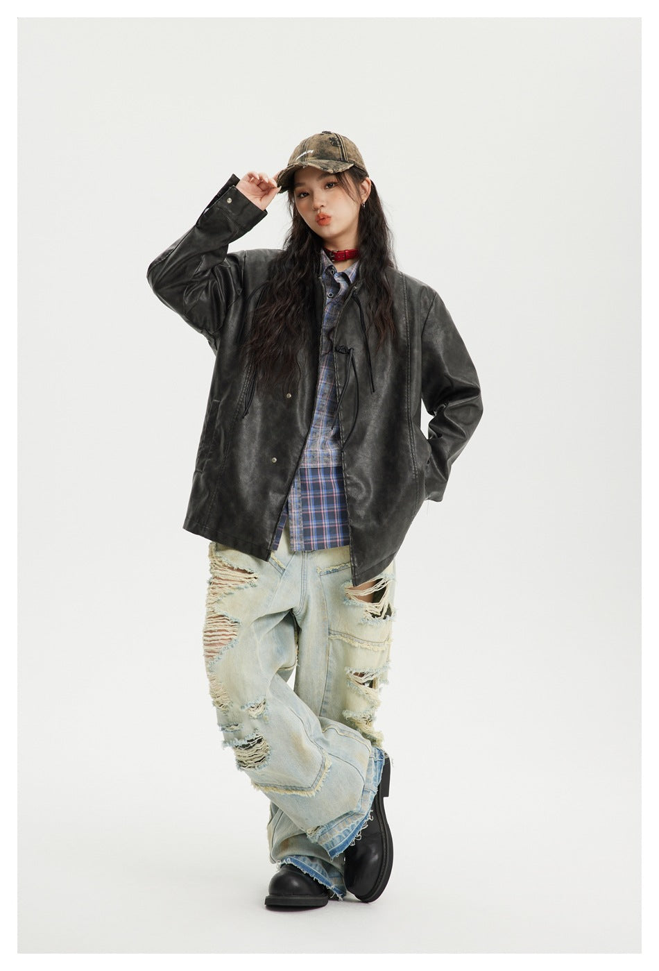 Model posing in a black jacket, blue plaid shirt, and distressed light-wash jeans.