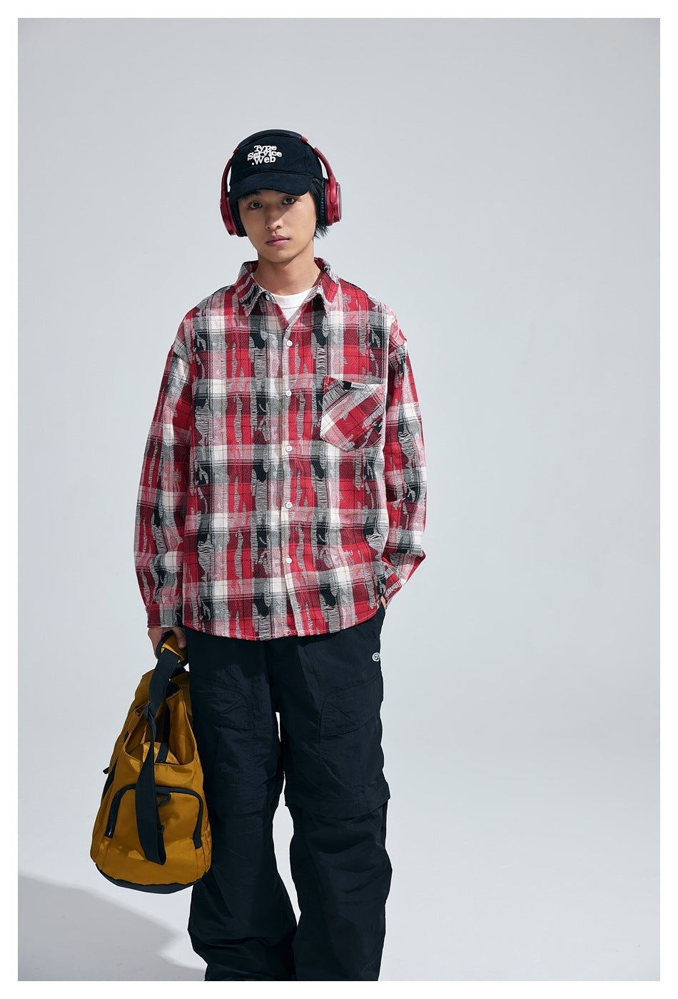 Model wearing red plaid long-sleeve shirt with chest pocket, black cap, red headphones and black cargo pants