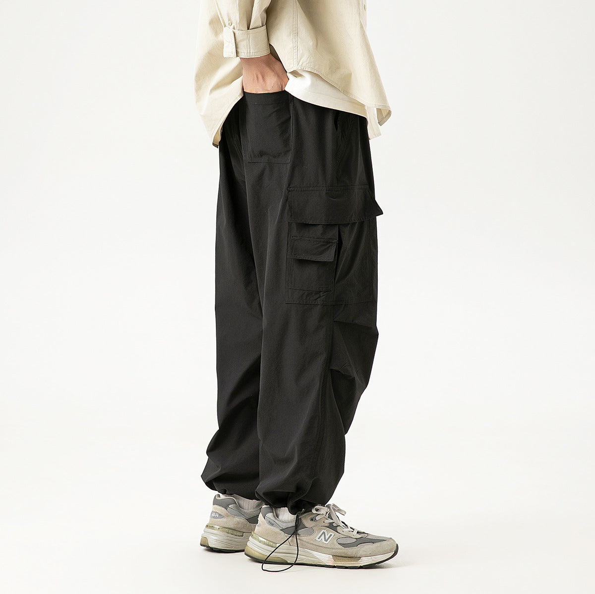 Model wearing loose black cargo pants with layered side pockets, shown from the side.