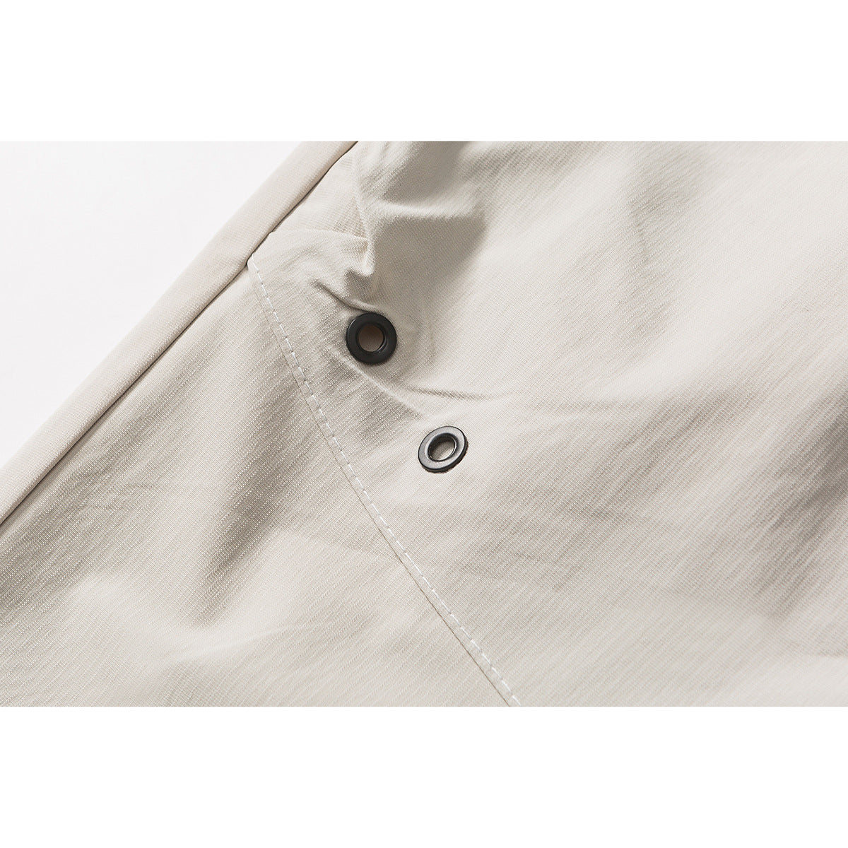 Close-up of two dark metal eyelets set into light beige shorts fabric.