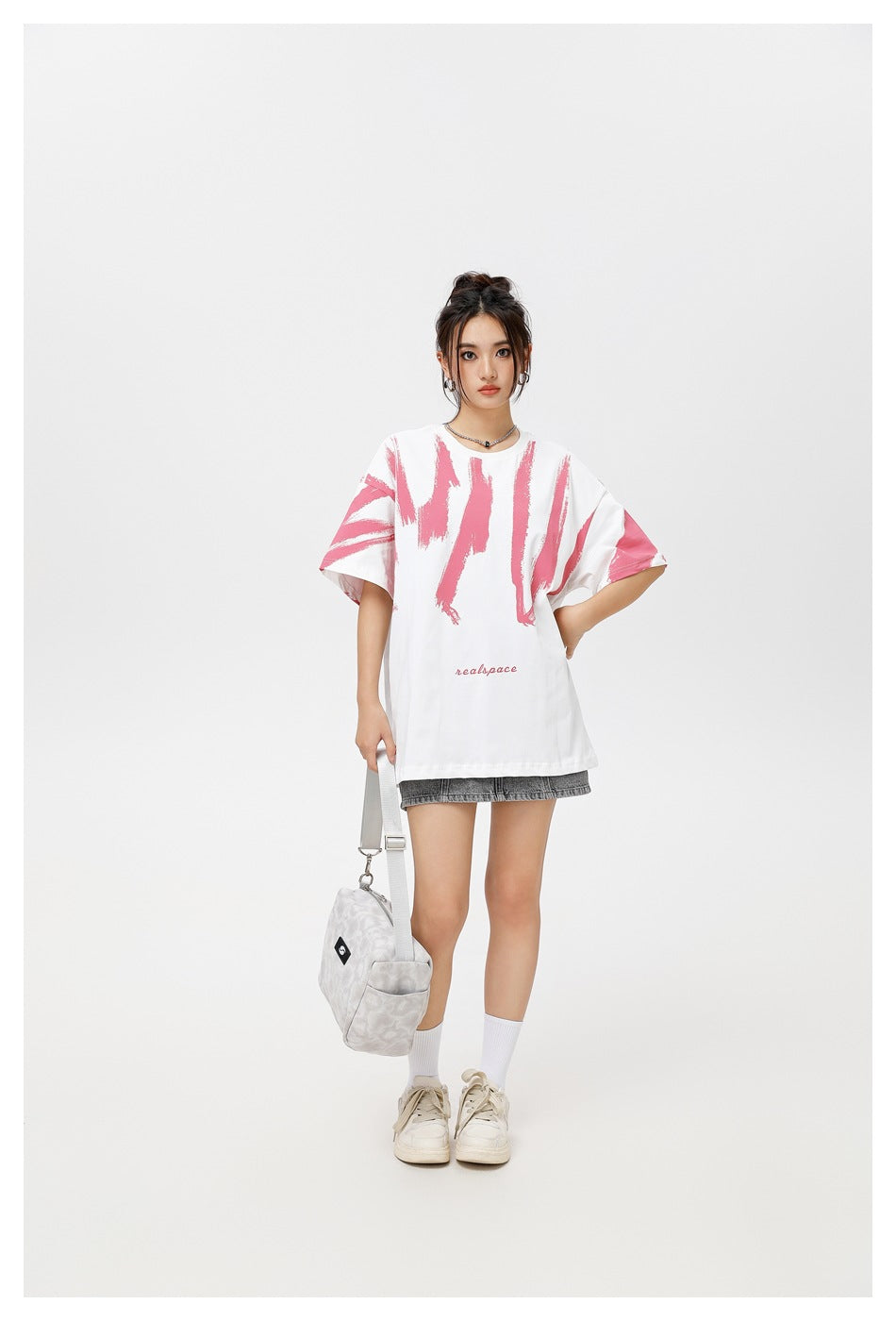 Full-length front view of a model wearing an oversized white T-shirt with pink brushstroke graphics and a gray skirt.