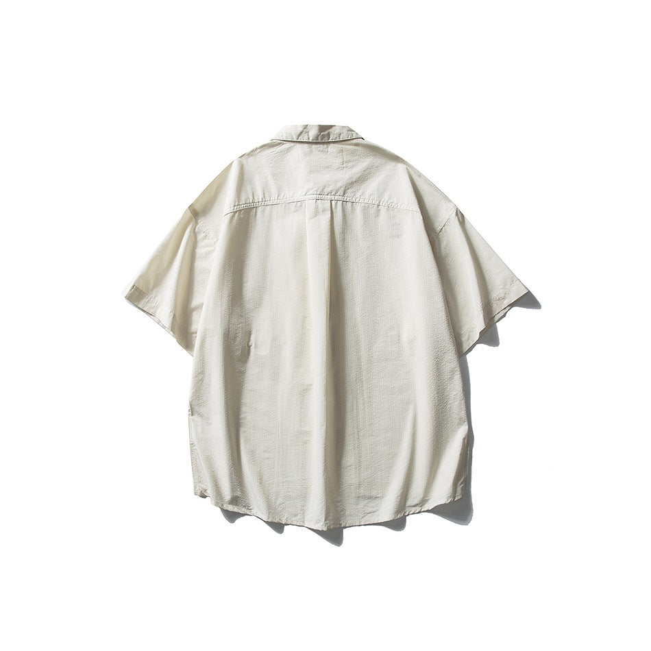 Back view of an off-white short-sleeve collared shirt with a center pleat and curved hem, displayed against white.