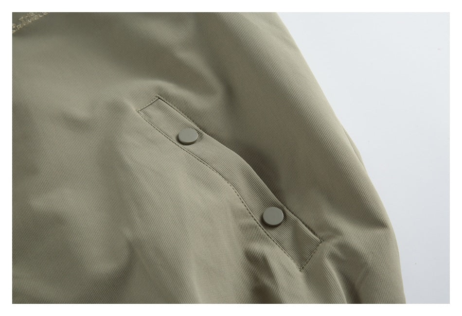 Close-up of an angled pocket flap with two round snap buttons on an olive-gray jacket.