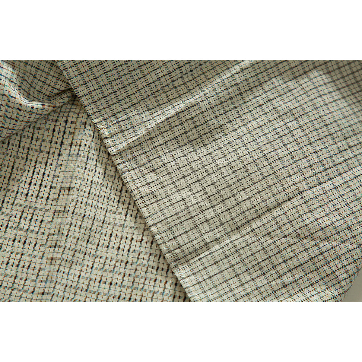 Close-up of cream plaid shirt fabric with a stitched edge and curved hem detail.