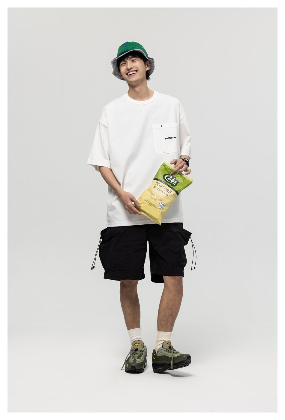 Full-length model in a white pocket T-shirt and black shorts, holding a snack bag.