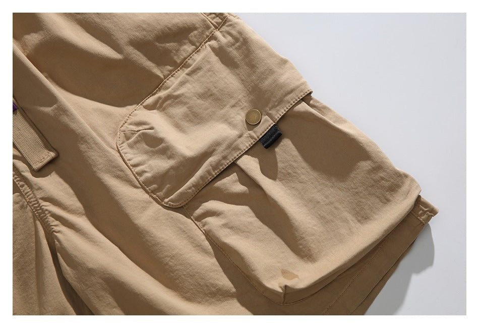 Close-up of the tan shorts' flap cargo pocket, showing its snap button and small black tab.