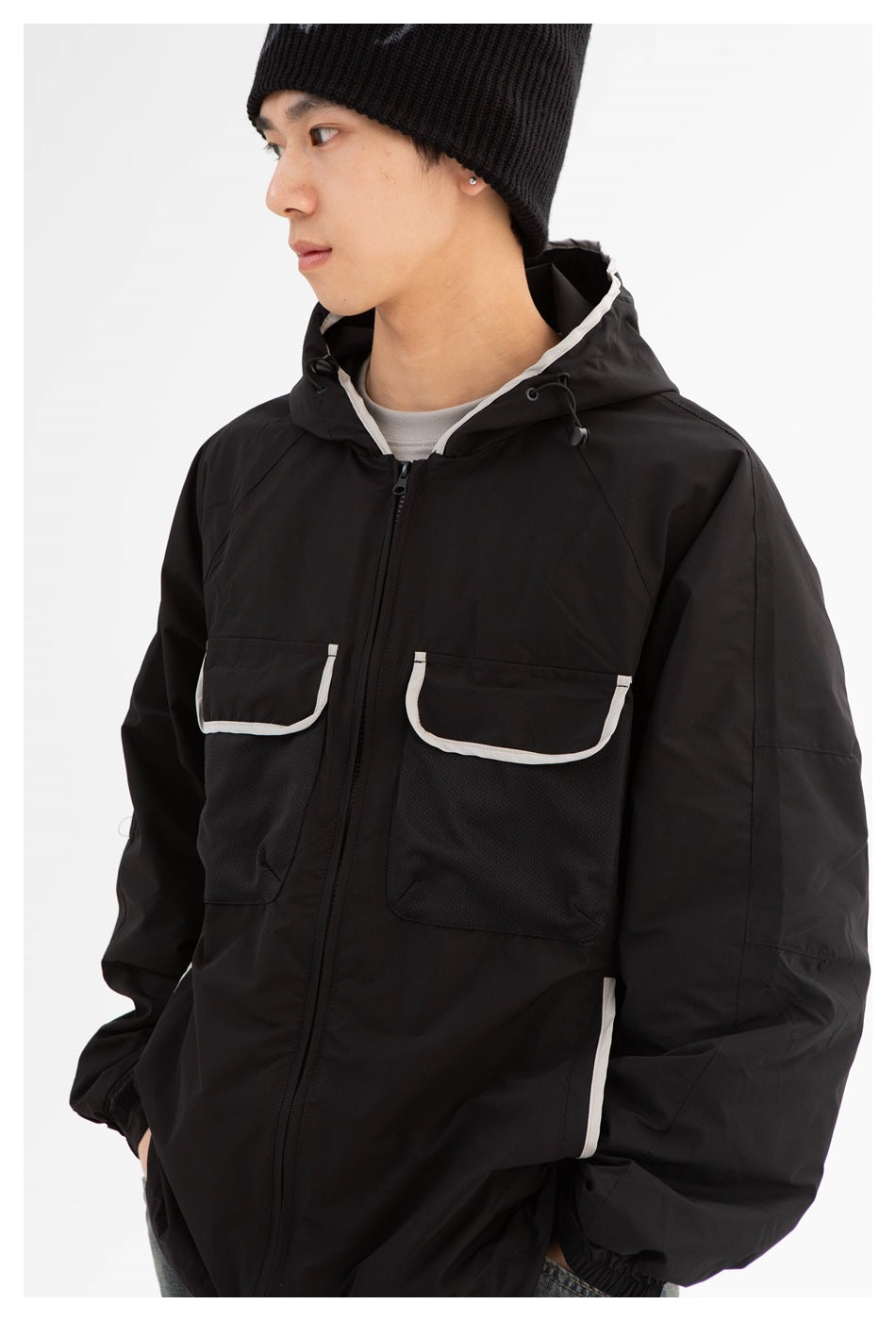 Front three-quarter view of a person wearing a black hooded jacket with white-trimmed chest pockets.