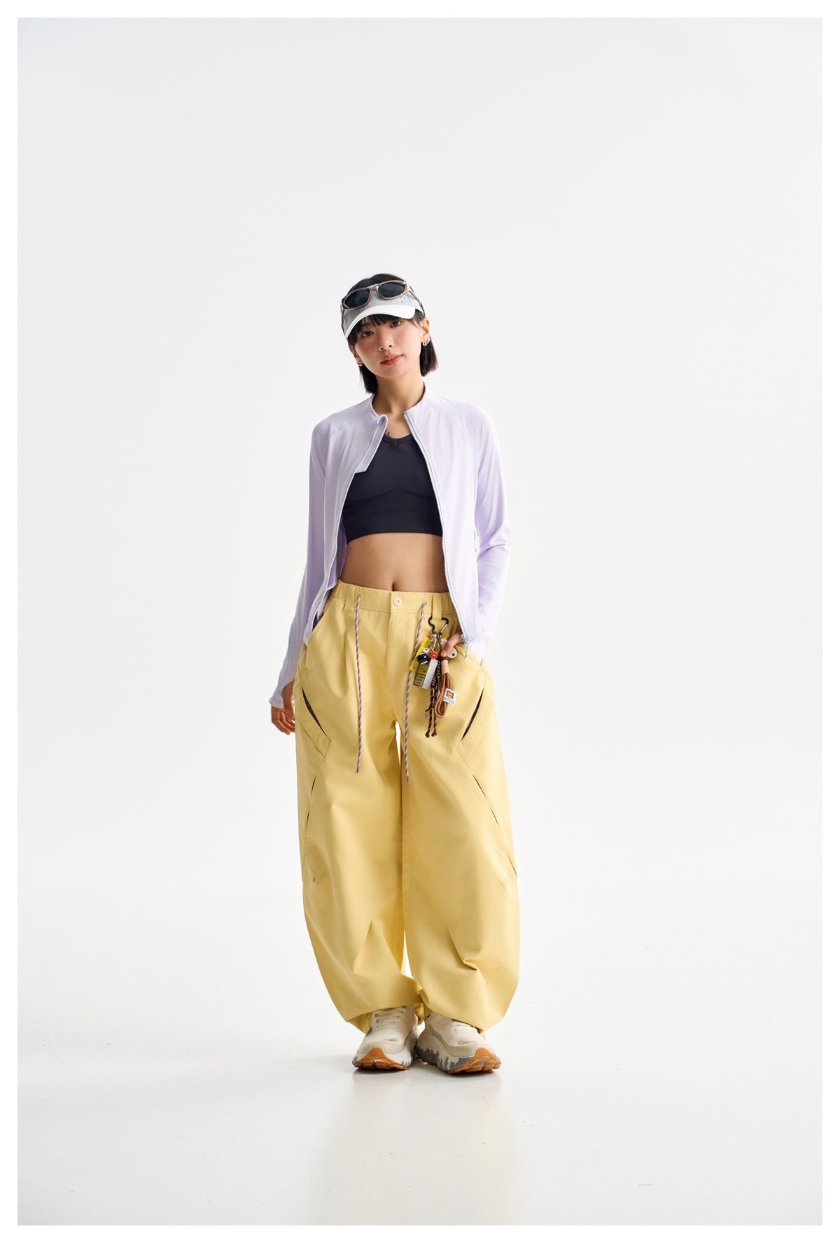Model wearing an open pale lavender jacket over a black crop top with loose yellow trousers.