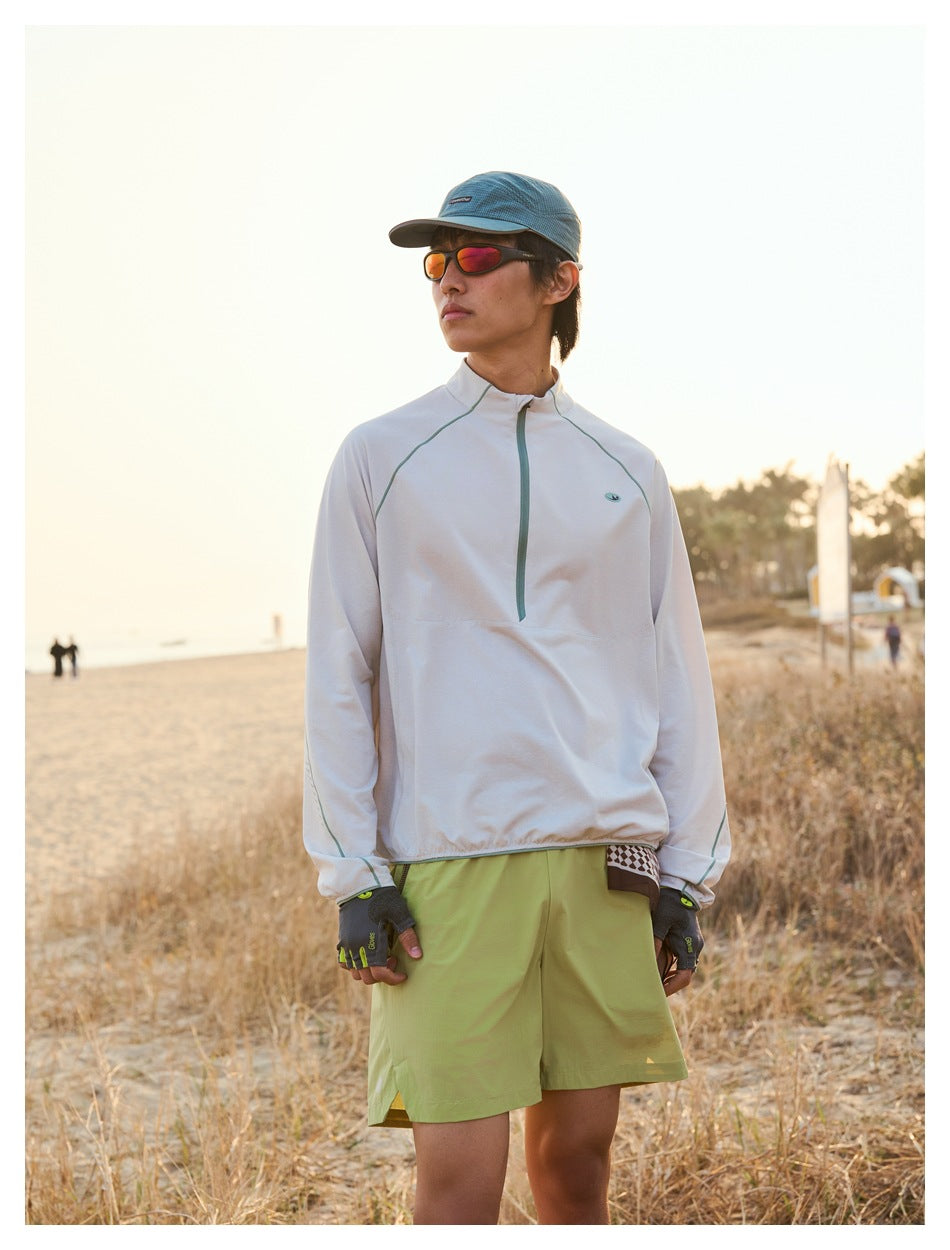 Front view of a man wearing a pale beige quarter-zip top and olive shorts on a beach.
