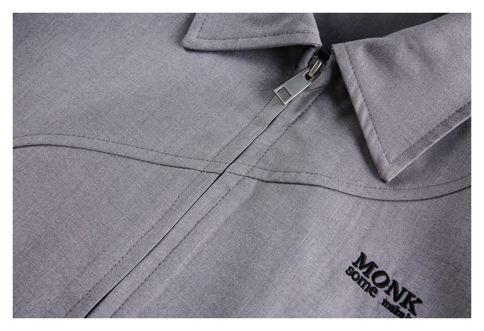 Close-up of a gray garment's collar, zipper, stitching, and black embroidered lettering.