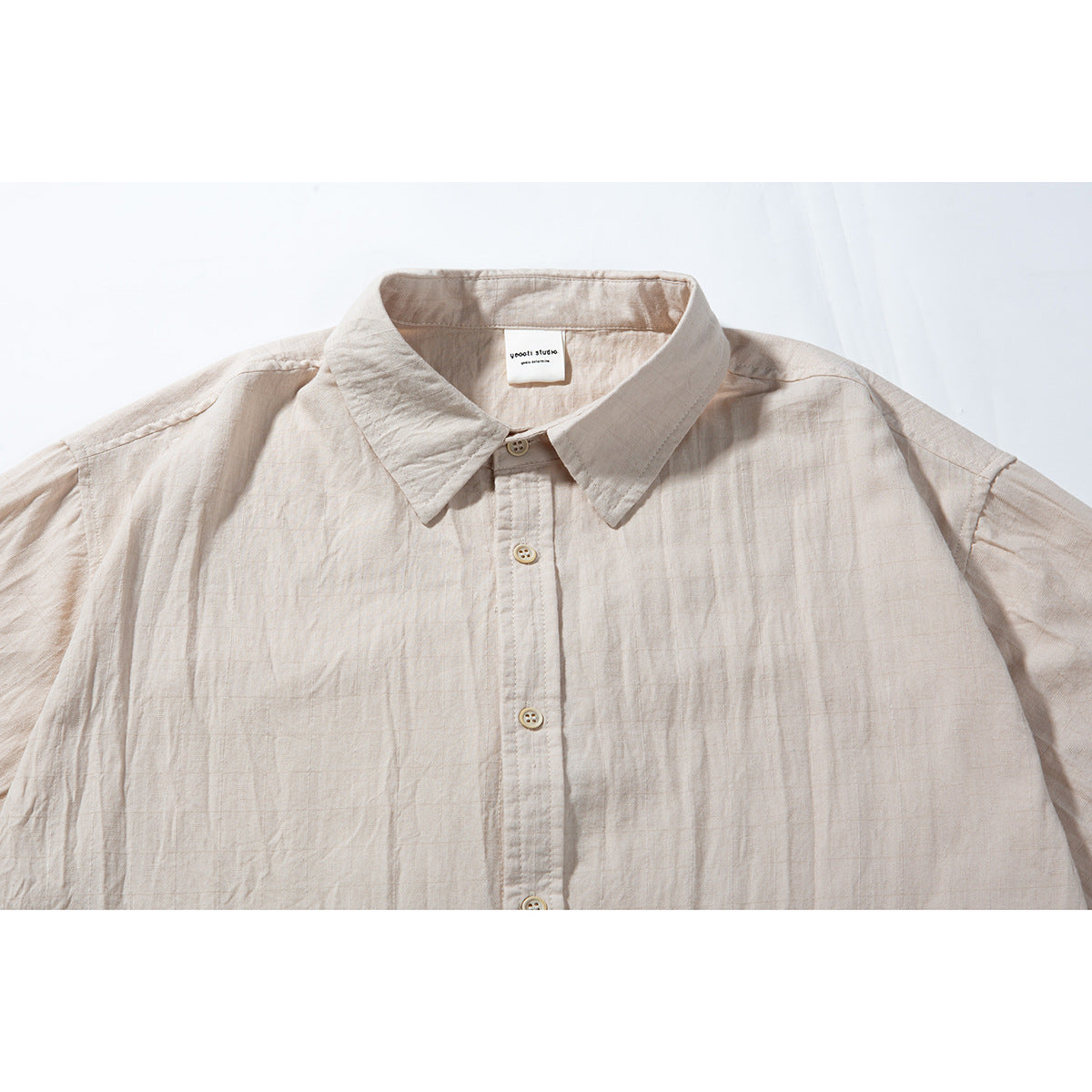 Close-up of a pale beige short-sleeve shirt showing its pointed collar, button placket, and subtle woven grid texture.