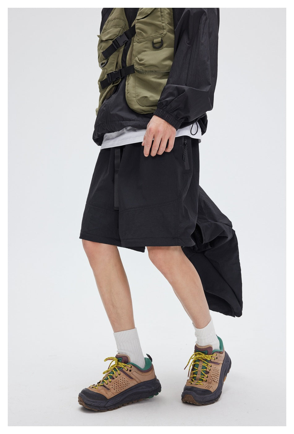 Cropped model wearing black knee-length shorts with a zip pocket, styled with a dark jacket and hiking shoes.