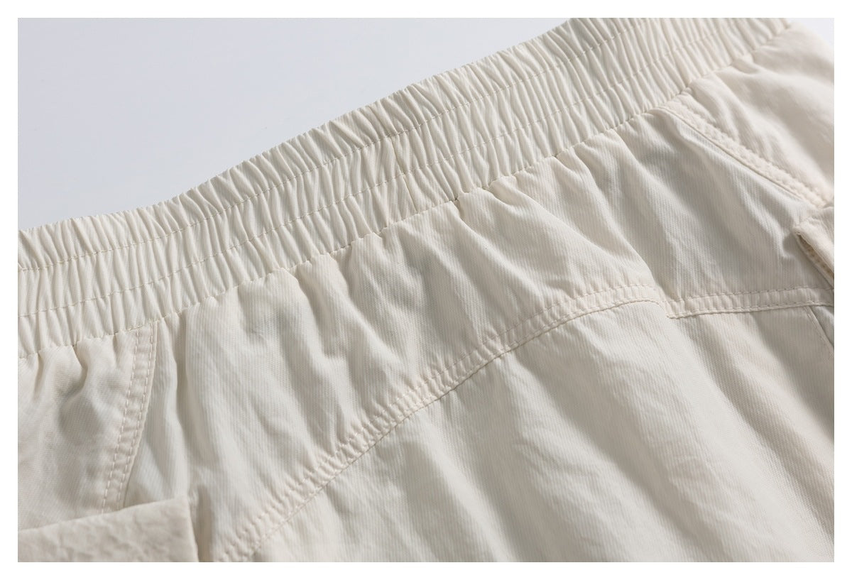 Close-up of cream shorts showing a gathered elastic waistband, curved stitching, and part of a pocket.
