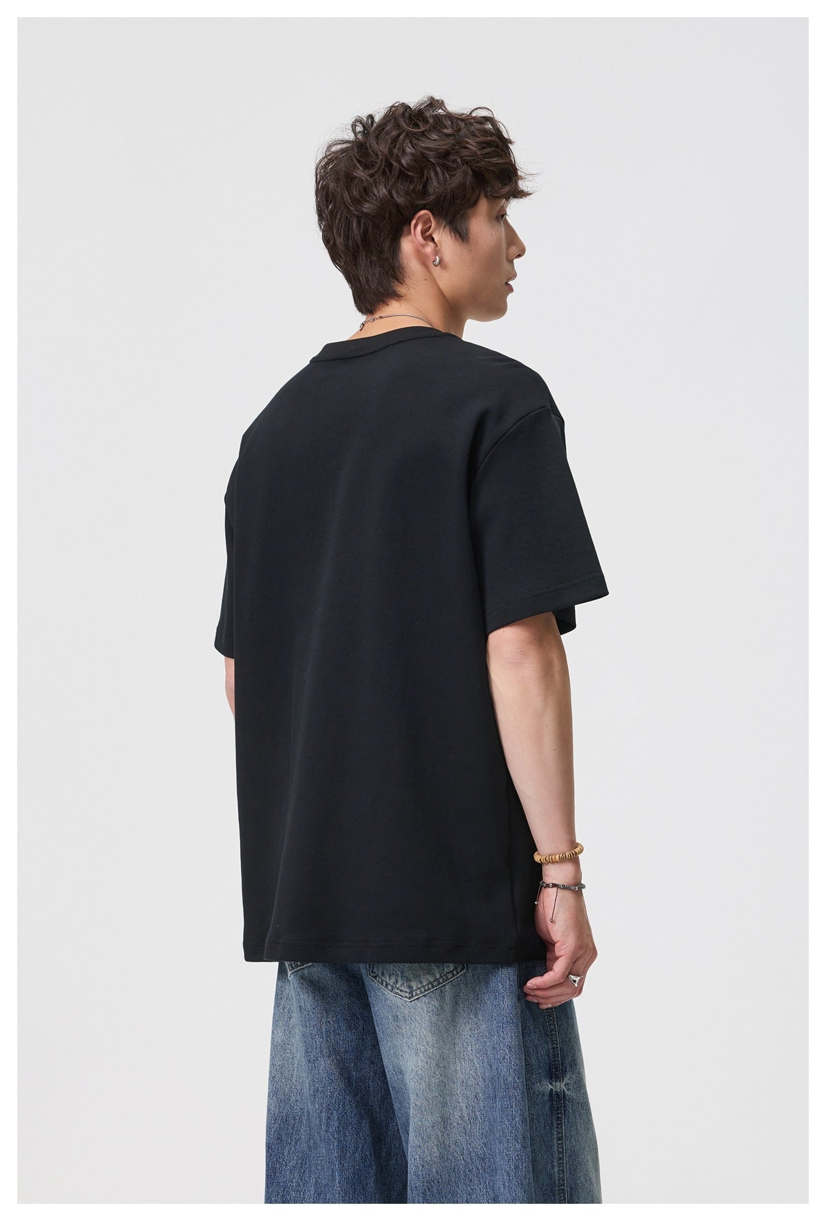 Rear three-quarter view of a model wearing an oversized plain black T-shirt.