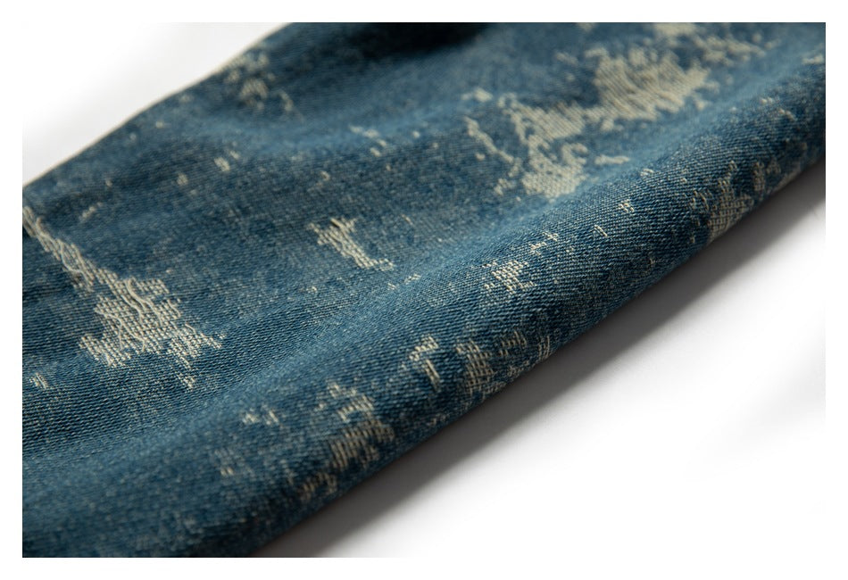 Close-up of a folded leg of distressed blue denim showing its pale pattern and stitched edge.