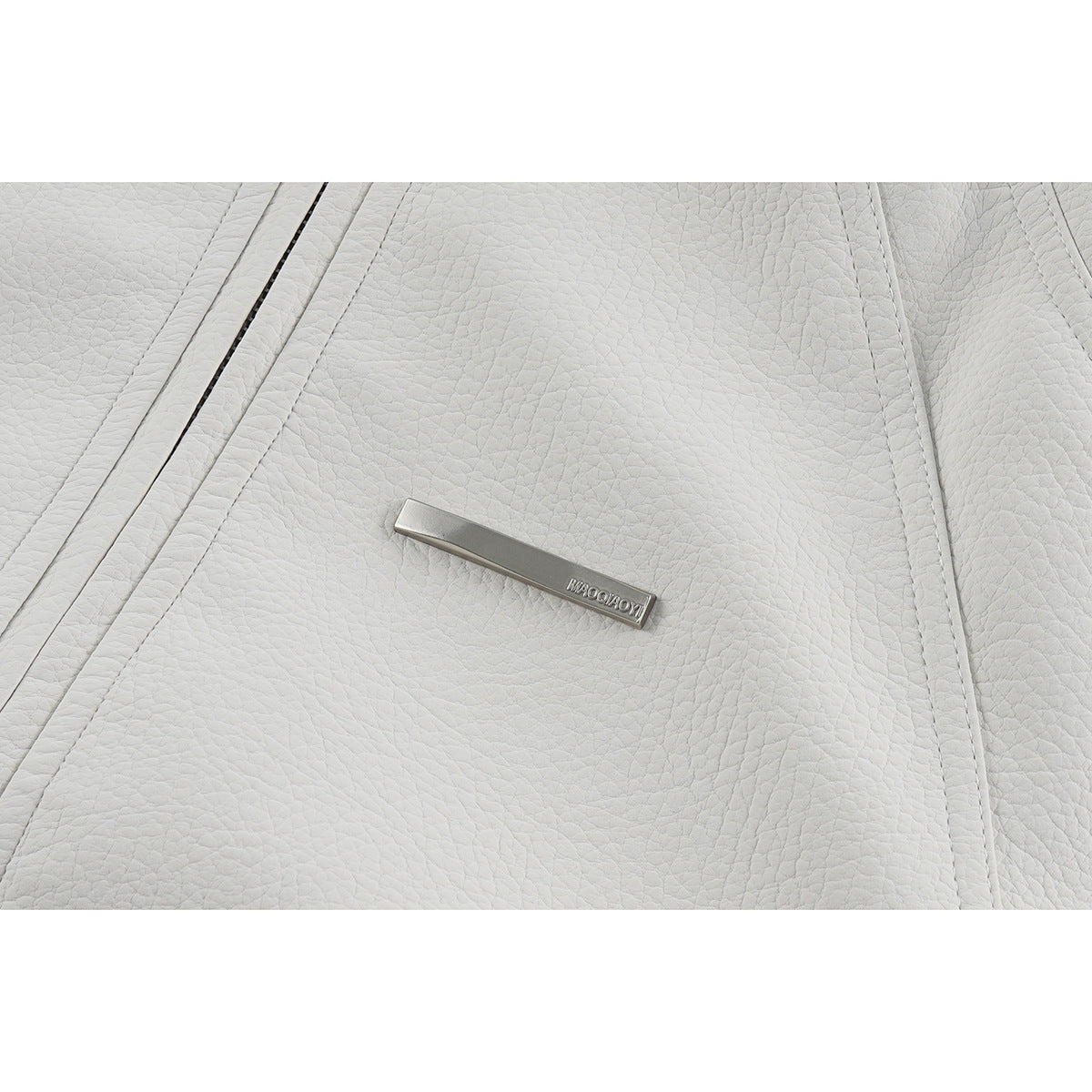 Close-up of off-white pebbled jacket material, seam stitching and a small metal chest plaque.