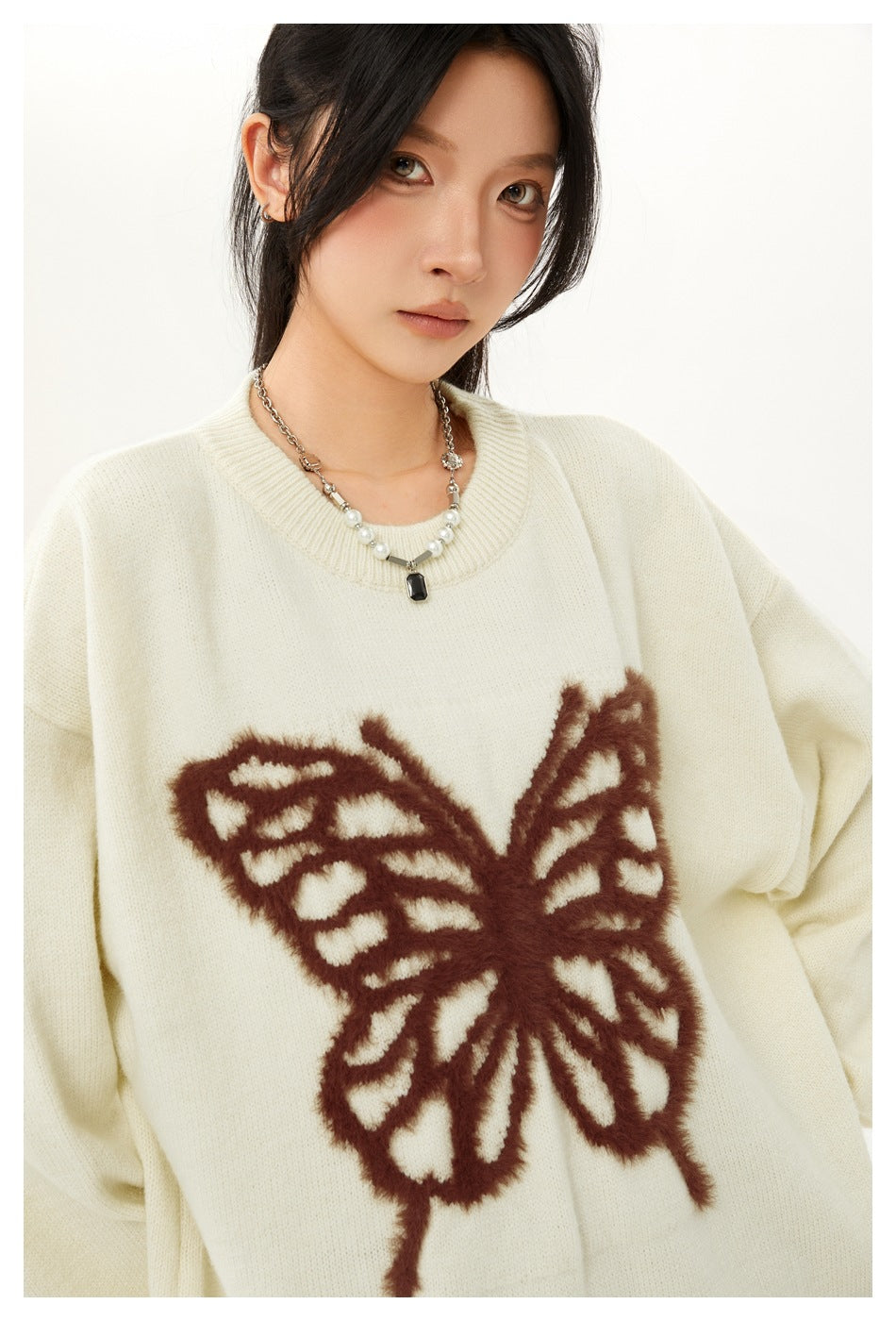 Close-up of a model wearing an ivory sweater with a large fuzzy brown butterfly motif and a ribbed crew neckline.