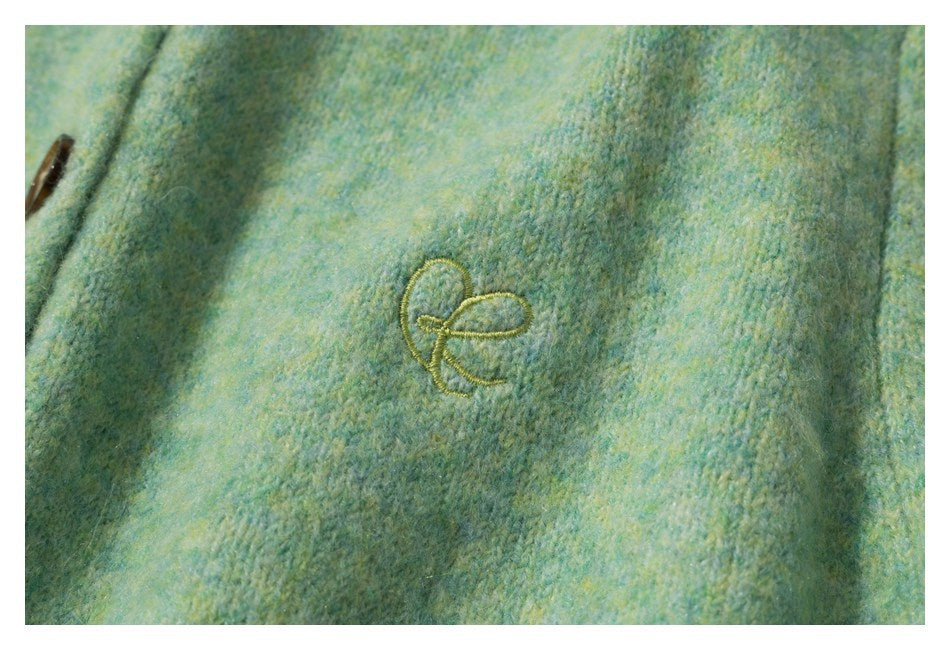 Close-up of a small embroidered motif and knit texture on a mint green mottled cardigan.