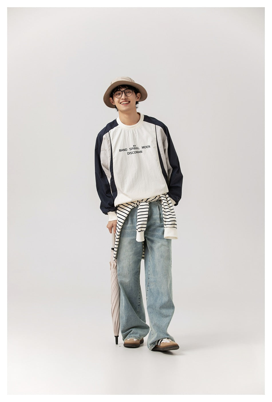 Model wearing an ivory and navy color-block top with black chest lettering, styled with loose jeans and a striped layer.