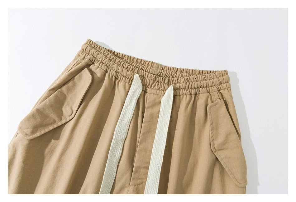 Close-up of tan pants with an elastic waistband, white drawstrings, and angled flap pockets.