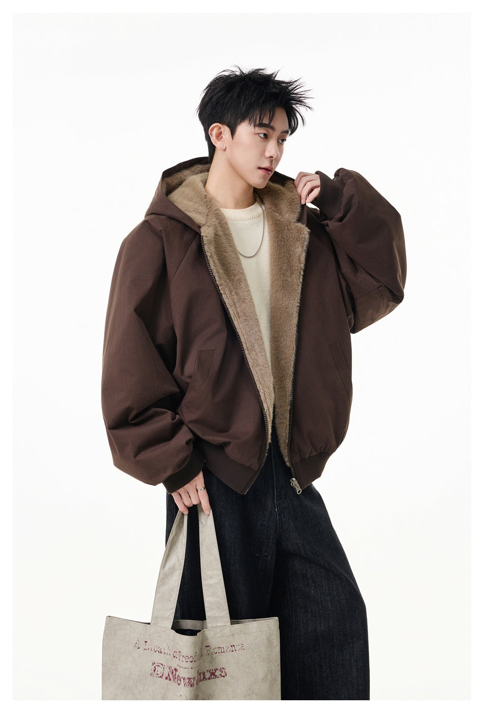 Model wearing an open dark brown hooded jacket with tan plush lining and carrying a light canvas tote.