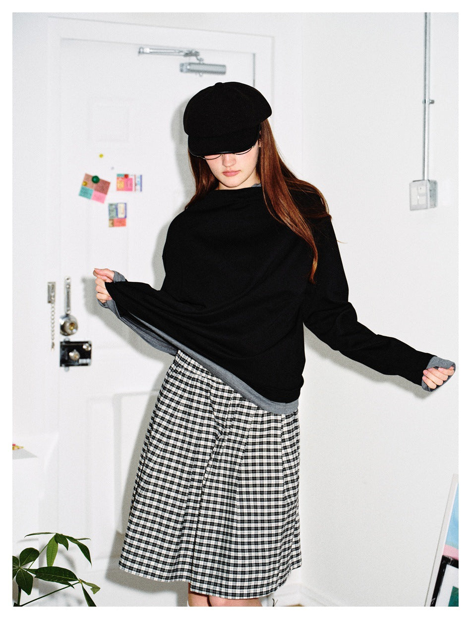 Woman wearing black top with gray layered hem and cuffs, styled with a plaid skirt and black cap