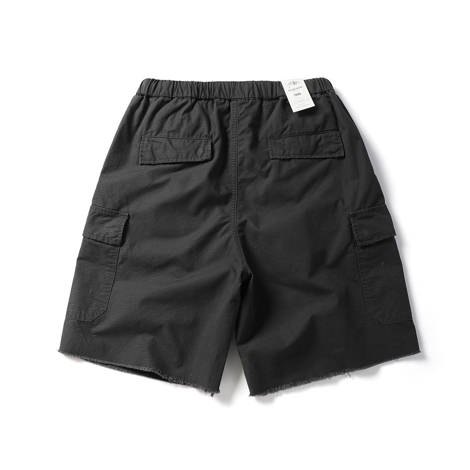 Back view of black cargo shorts with an elastic waistband, flap pockets, and raw-cut hems.
