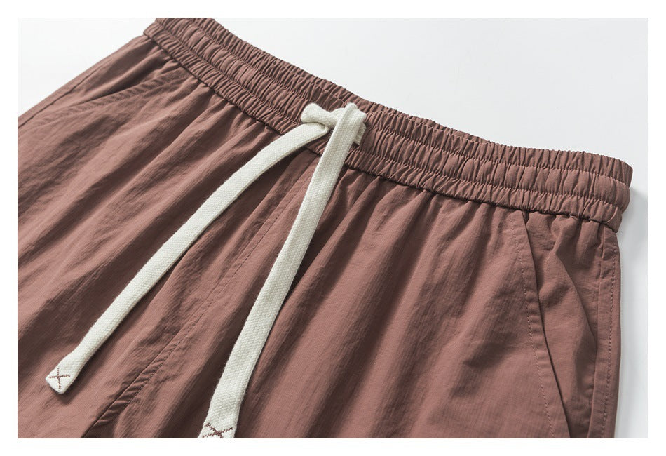 Close-up of dusty mauve shorts showing the gathered waistband, long white drawcords, and front pocket opening.