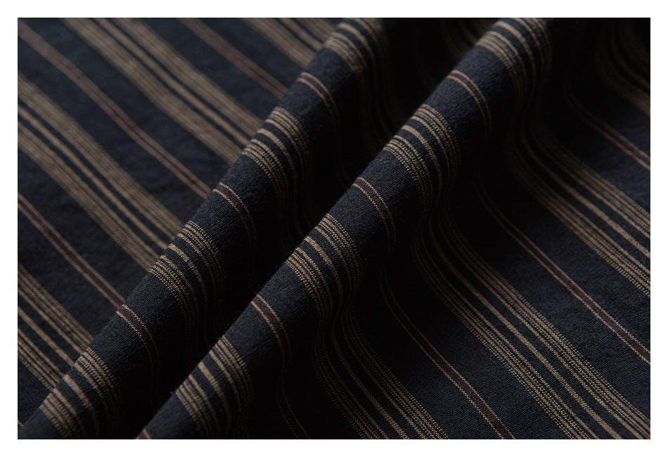 Close-up of dark fabric with narrow tan and muted brown stripes, draped into soft folds.
