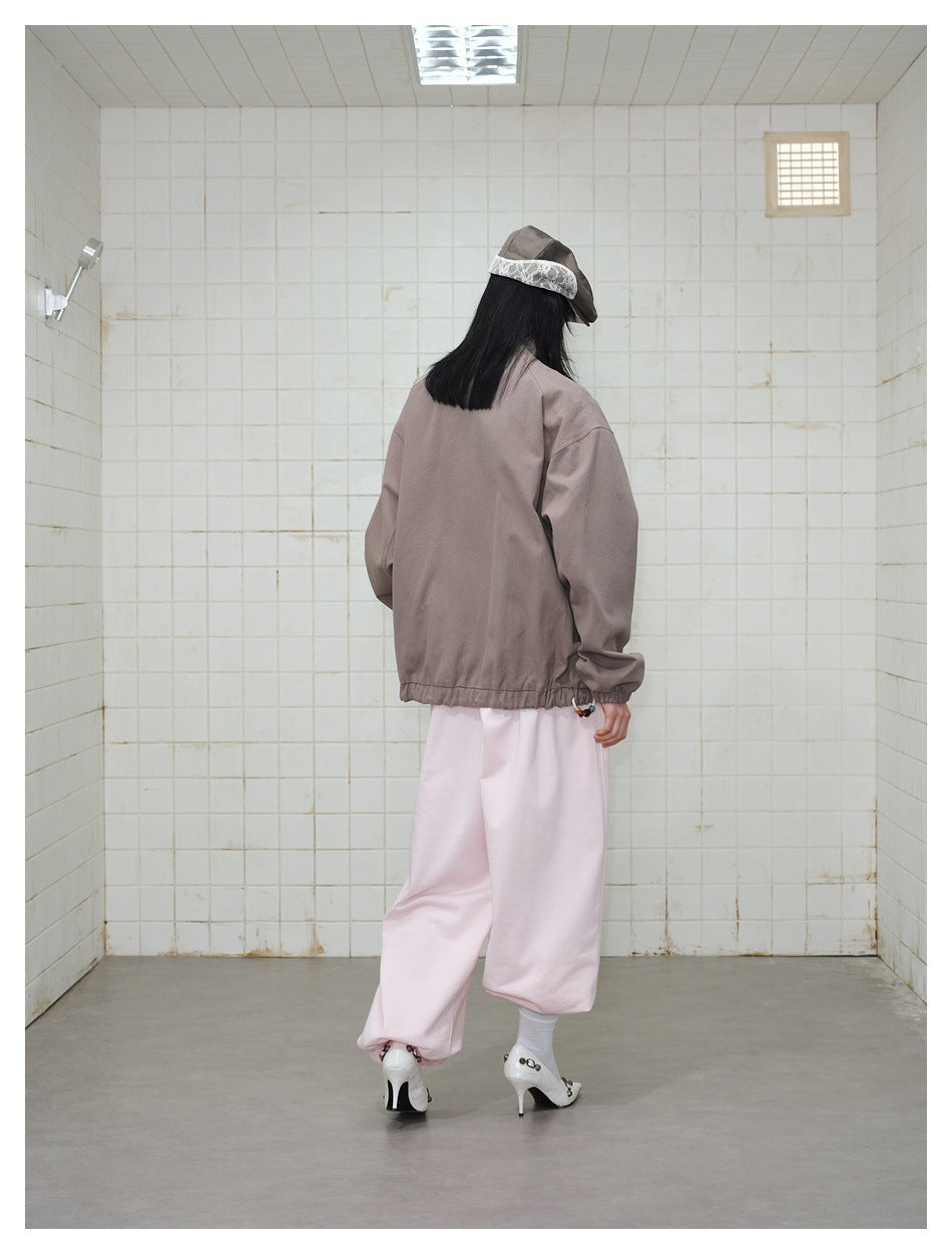Back view of a model wearing a plain taupe jacket, pale pink trousers, and a gray cap.